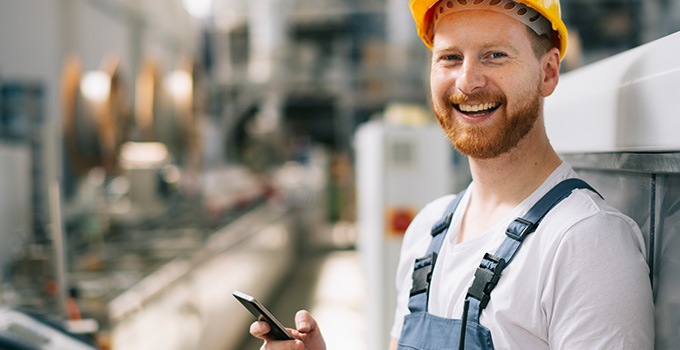 Happy factory worker holding a mobile phone.